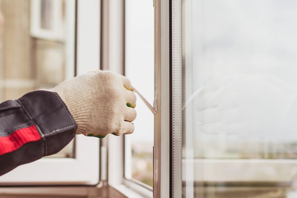Intervention de maintenance sur menuiserie intérieure, technicien équipé de gants de protection et veste de travail procédant à l'ajustement d'un châssis de fenêtre