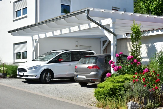 Scène extérieure d'une maison moderne avec garage, voiture blanche stationnée sur béton lissé, ciel bleu dégagé, architecture contemporaine aux lignes épurées