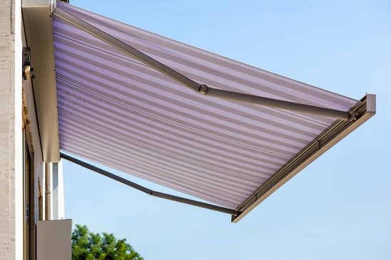 Ouvrier en salopette rouge et casquette installant ou réparant un store à lamelles métalliques sur une terrasse couverte