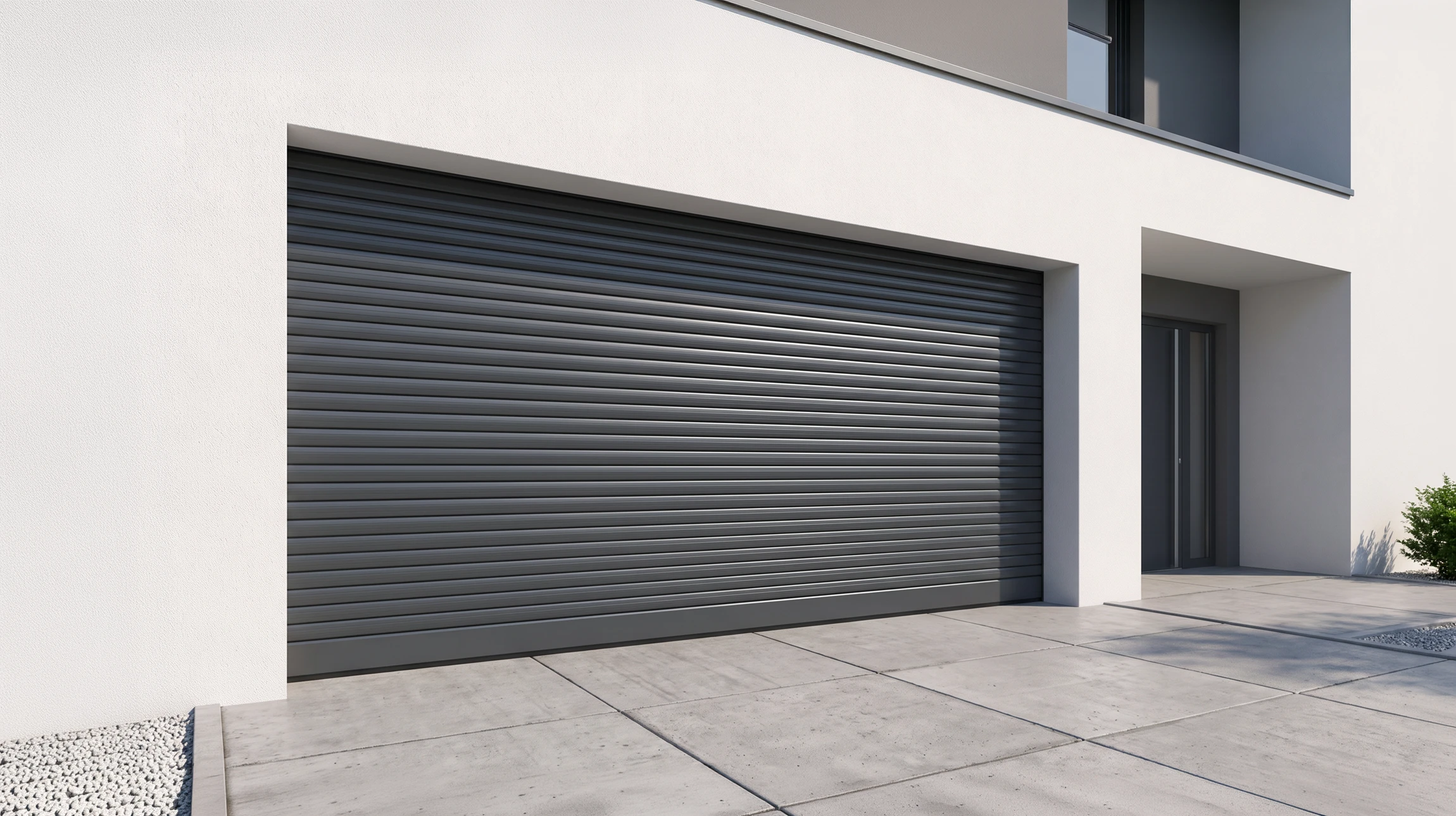 Façade d'une maison résidentielle contemporaine en enduit blanc ou brique, avec une porte de garage enroulable en aluminium gris anthracite partiellement ouverte (environ 50% levée), révélant l'intérieur du garage et l'espace libéré. Le tablier à lames horizontales en aluminium est clairement visible en cours de levée vers le linteau. Un véhicule SUV gris est visible à proximité, stationné devant. Les guidages latéraux et le caisson de la porte sont apparents. L'environnement résidentiel (pelouse, jardin paysager, façade moderne) renforce le contexte familial et contemporain. La mise en scène privilégie la démonstration du gain d'espace de la solution enroulable.