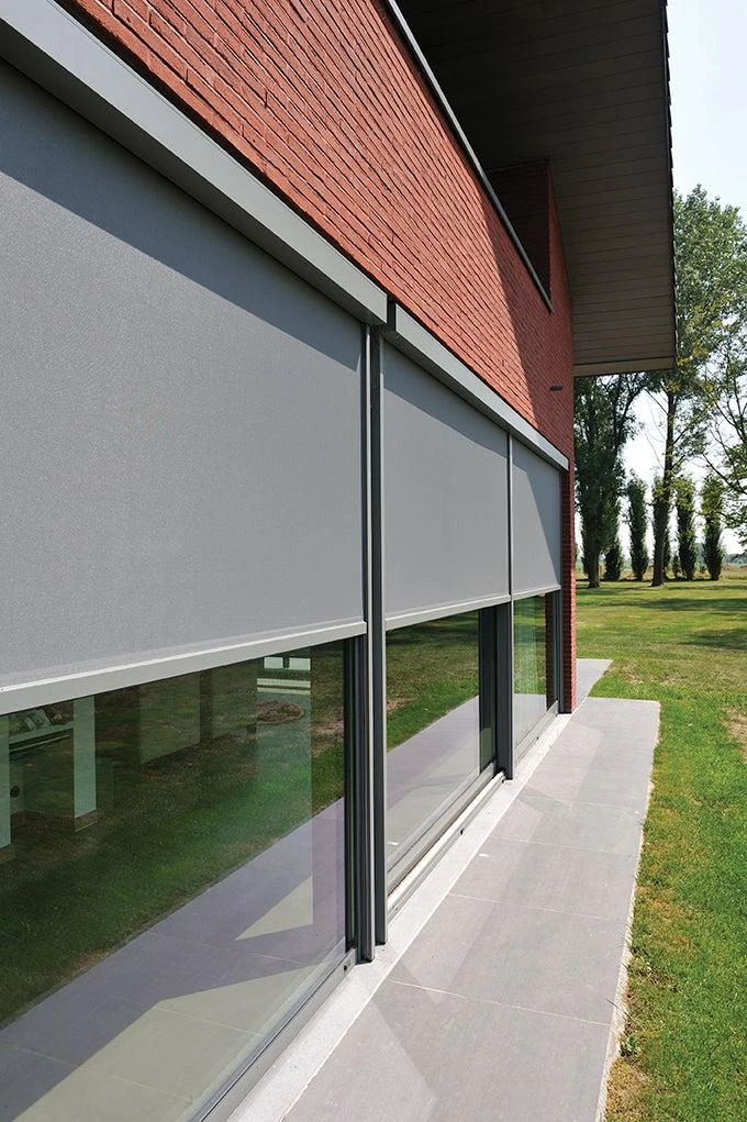 Façade en brique avec deux fenêtres équipées de volets roulants métalliques couleur taupe, partiellement ouverts
