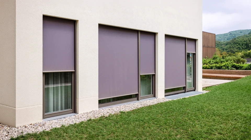 Façade extérieure d'une maison méditerranéenne avec une fenêtre équipée d'un volet roulant aluminium blanc partiellement descendu et de volets battants aluminium gris-bleu ouverts
