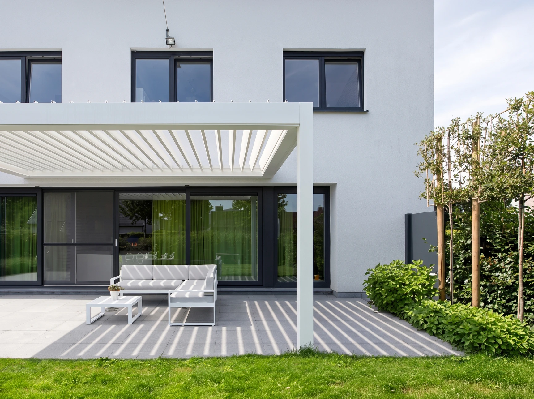Façade latérale d'une maison contemporaine en briques beiges, avec deux fenêtres à cadres anthracite équipées de caissons de volets roulants intégrés